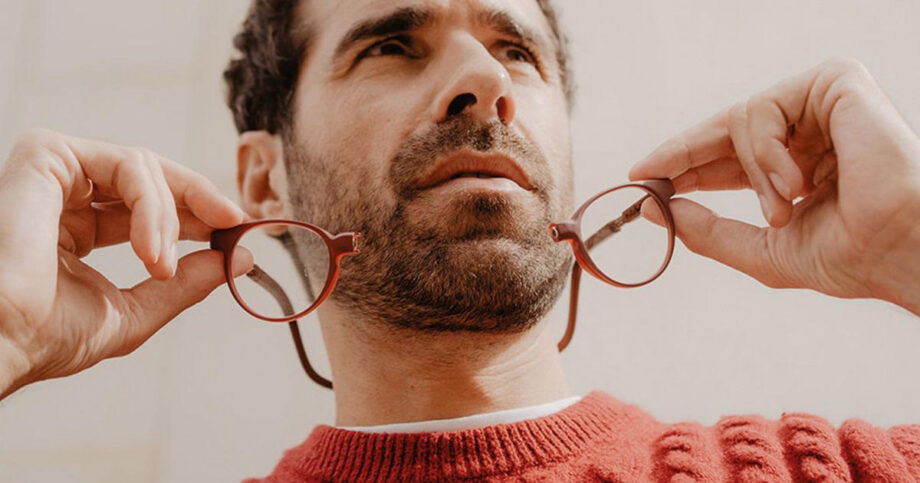 Uomo con maglione rosso che tiene in mano degli occhiali da lettura magnetici rossi aperti sul ponte frontale.